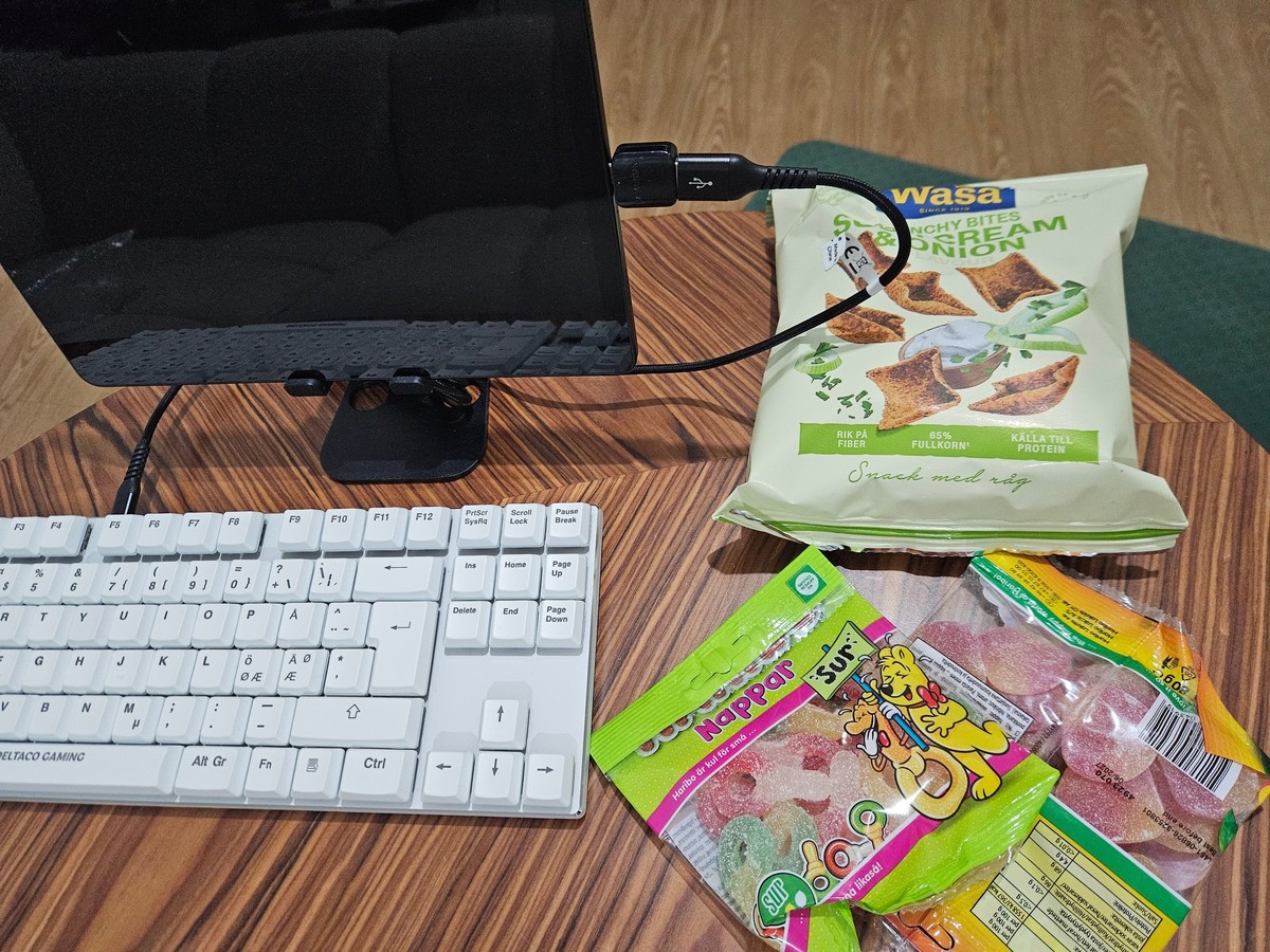An image showing a physical keyboard attaches to a tablet with a USB-cable. Next to them to the right are one bag of rye potato chips and two bags of sour candy.