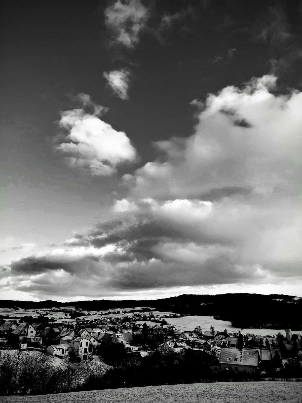 view of snow-covered village in rolling hills, focus is in clouds in the sky