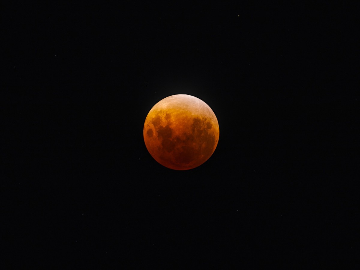 A full moon, tinted in orange and red, during the peak of the eclipse.  Stars are visible in the background of the night sky